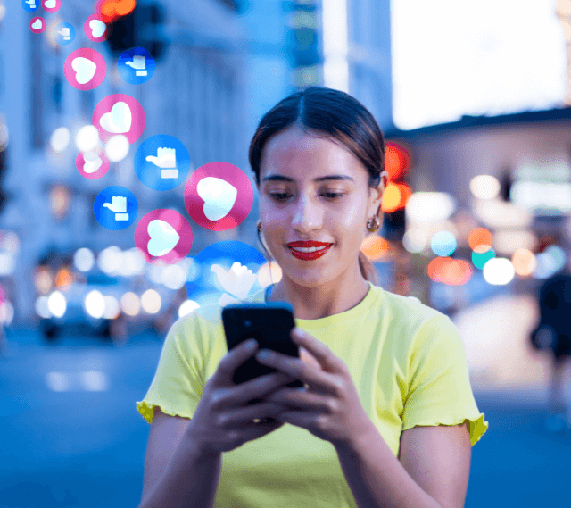 woman standing smiling and typing on her phone with like hearts and thumbs ups flowing from her phone